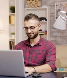 Handsome man laughing while working on laptop in living room